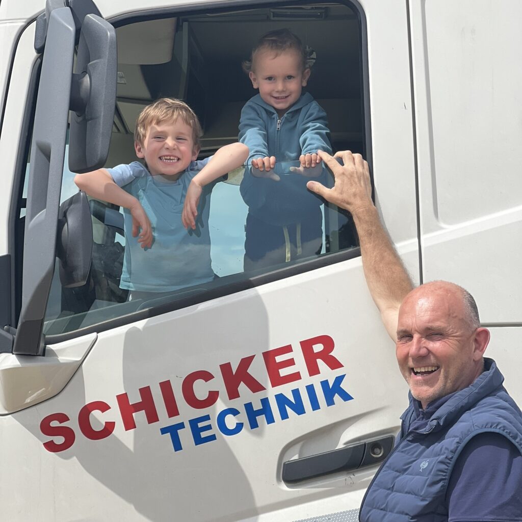 Zwei Kinder und Mann lächeln aus Lastwagenfenster.